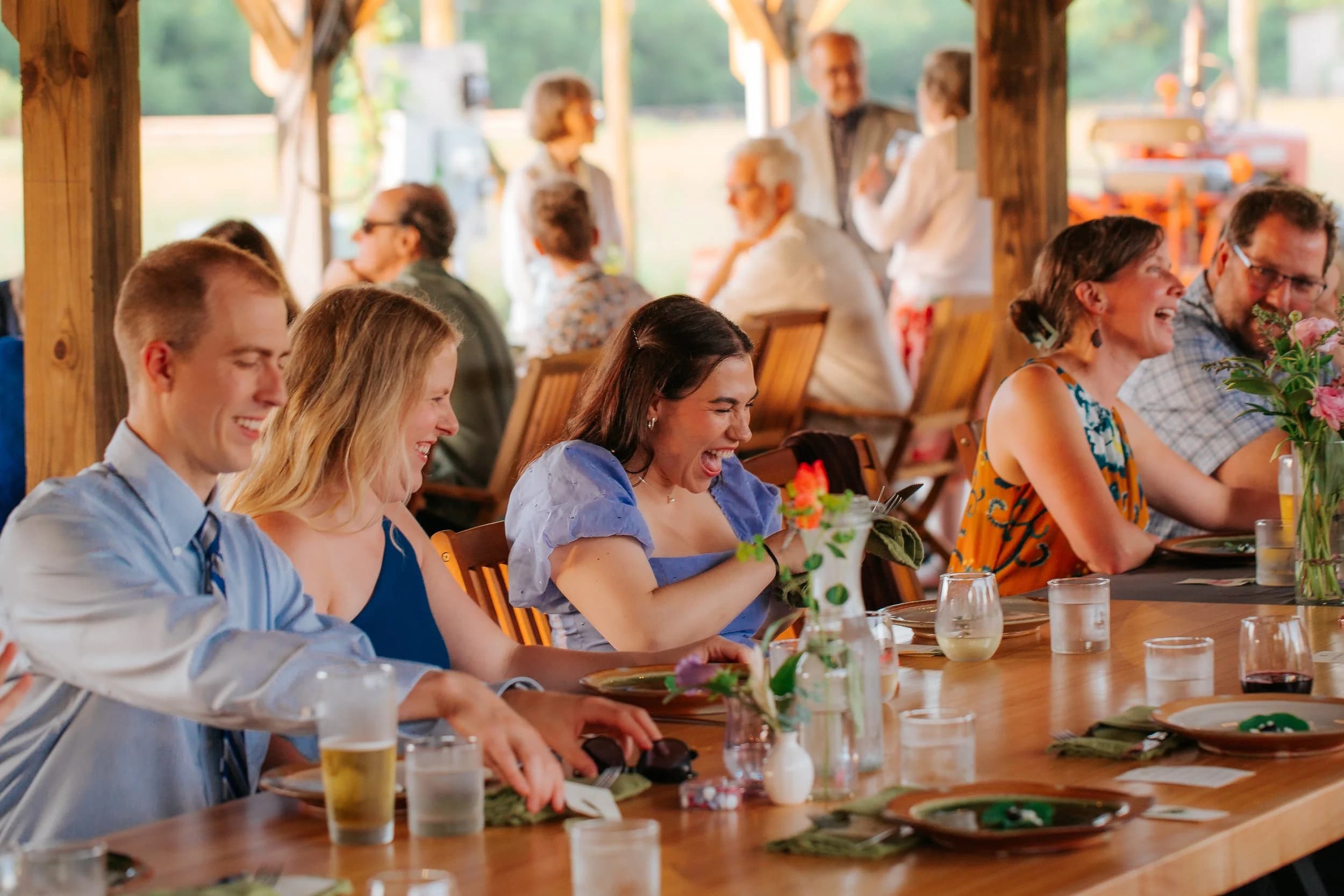 Guests laughing around a long reception table under the barn